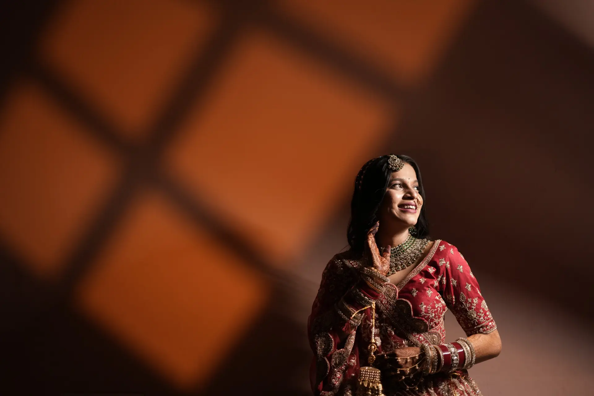 Bride in red wedding attire illuminated by an artistic warm spotlight