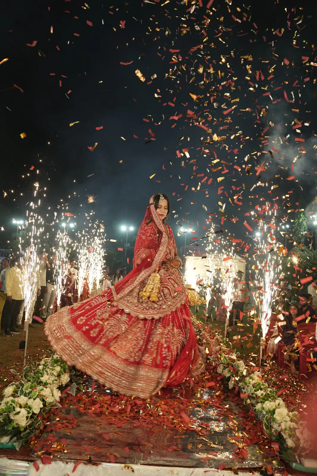Bride twirling in a red lehenga amid confetti and sparklers
